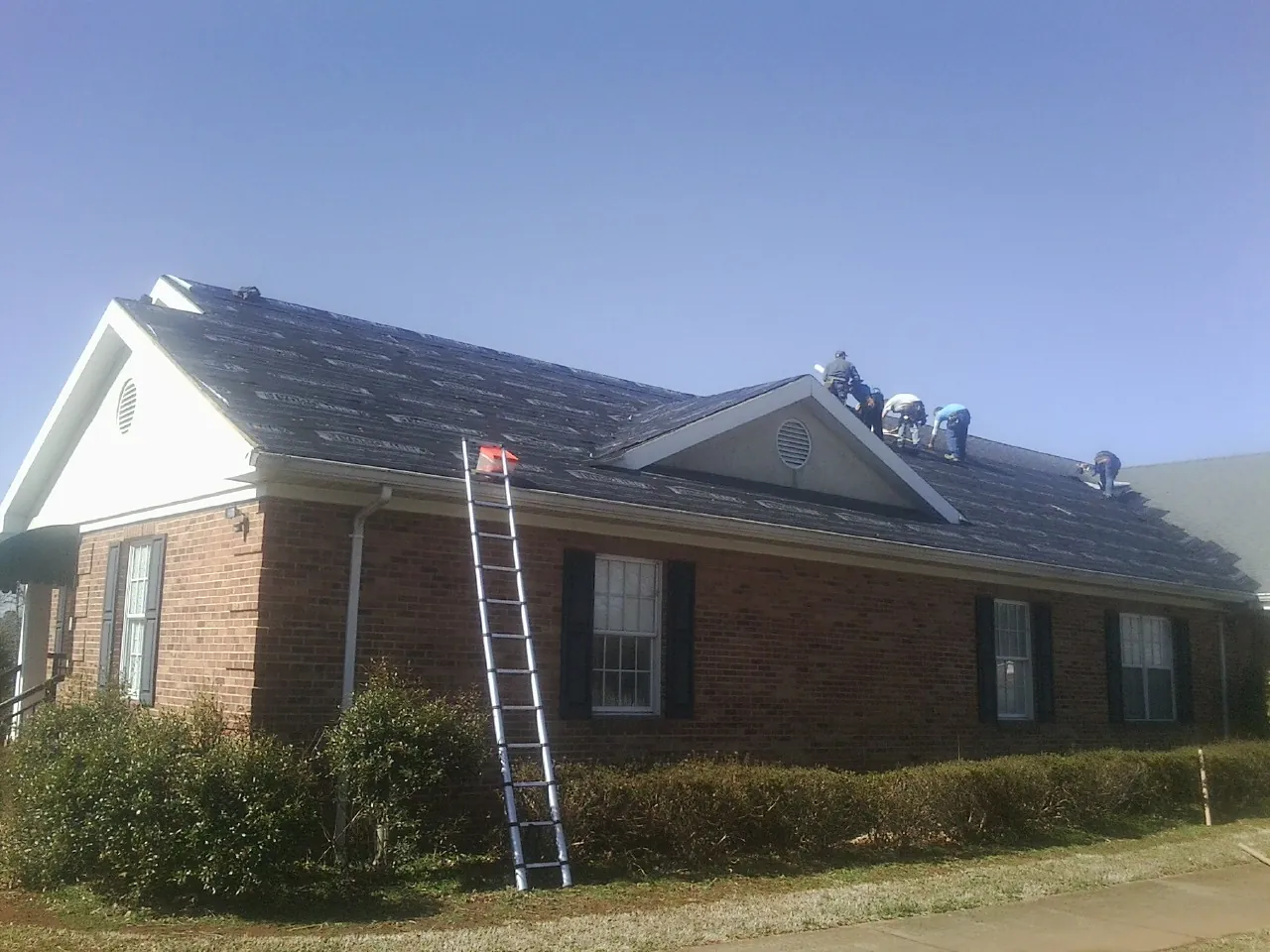 Crew tearing shingles off a brick ranch roof with a ladder set — Metal Roof Repair work by our crew in New Gretna