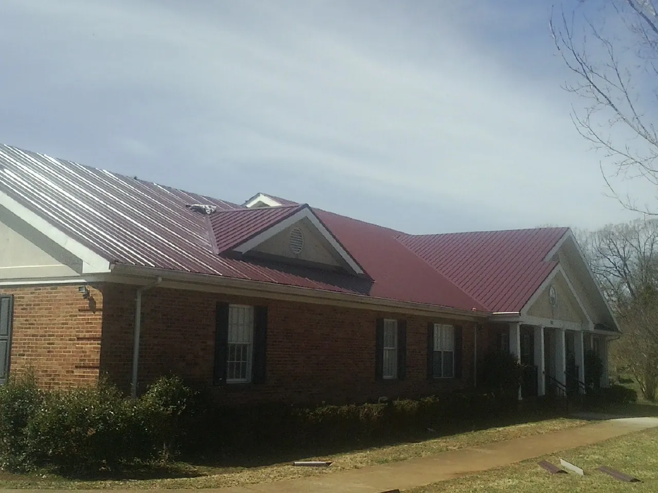 Red metal roof with gabled entries on a long brick building, from a Hail Damage Roof Repair job in New Gretna