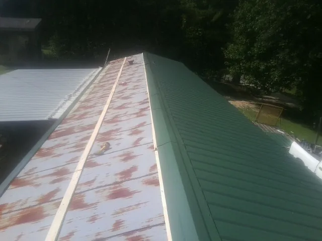 Old rusted panels beside newly installed green metal roofing — Wind Damage Roof Repair by Roofing Brothers in New Gretna