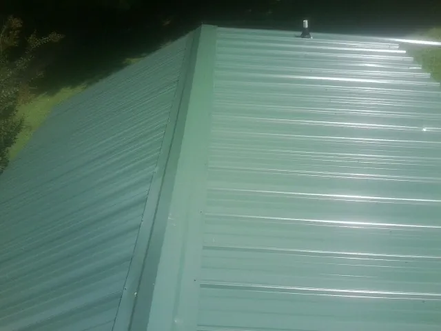 New green metal panels meeting at the ridge of a roof — Flat Roof Repair work by our crew in New Gretna