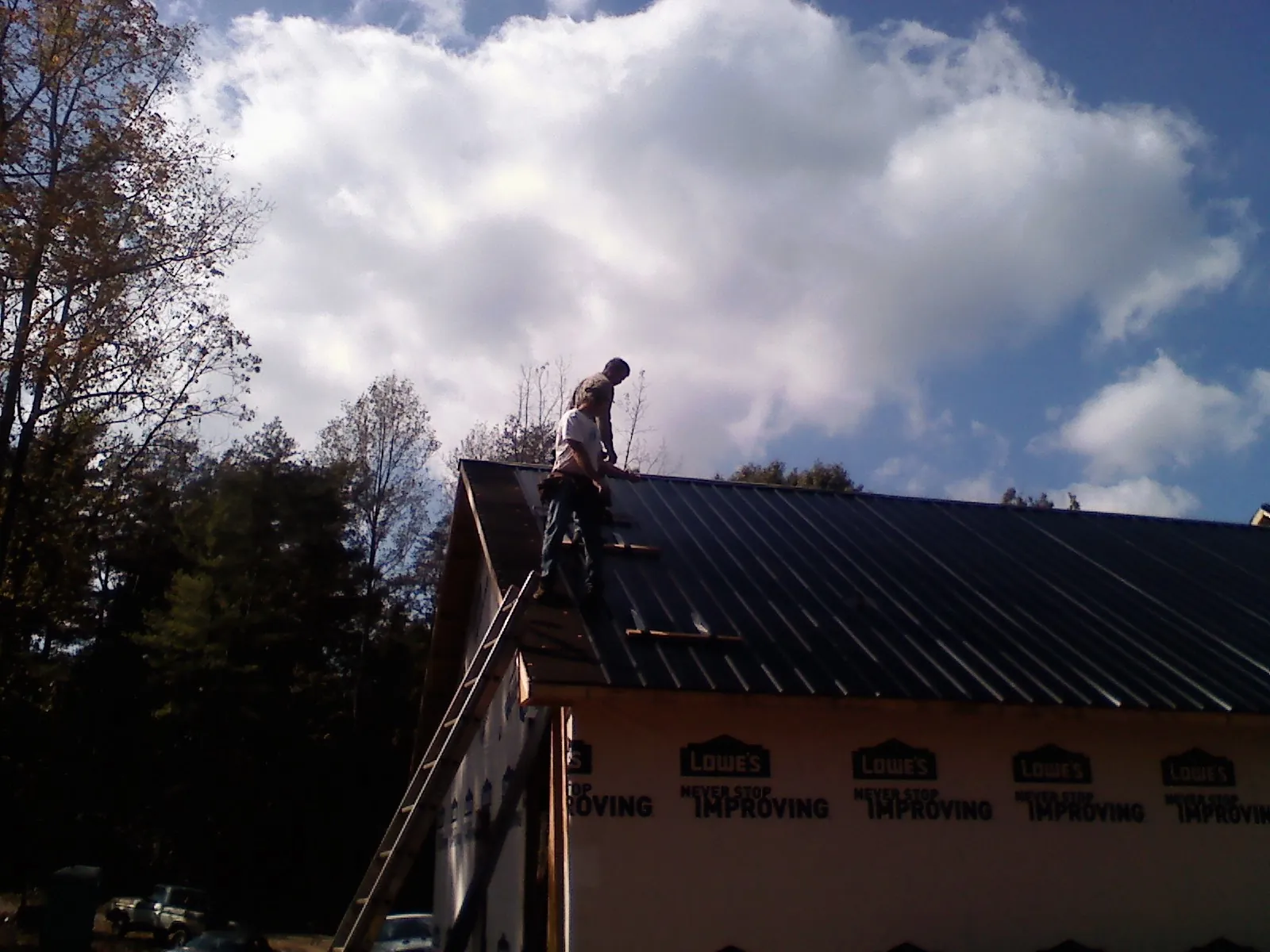 Roofer fastening dark metal panels high against a cloudy sky, from a Roof Inspection job in New Gretna