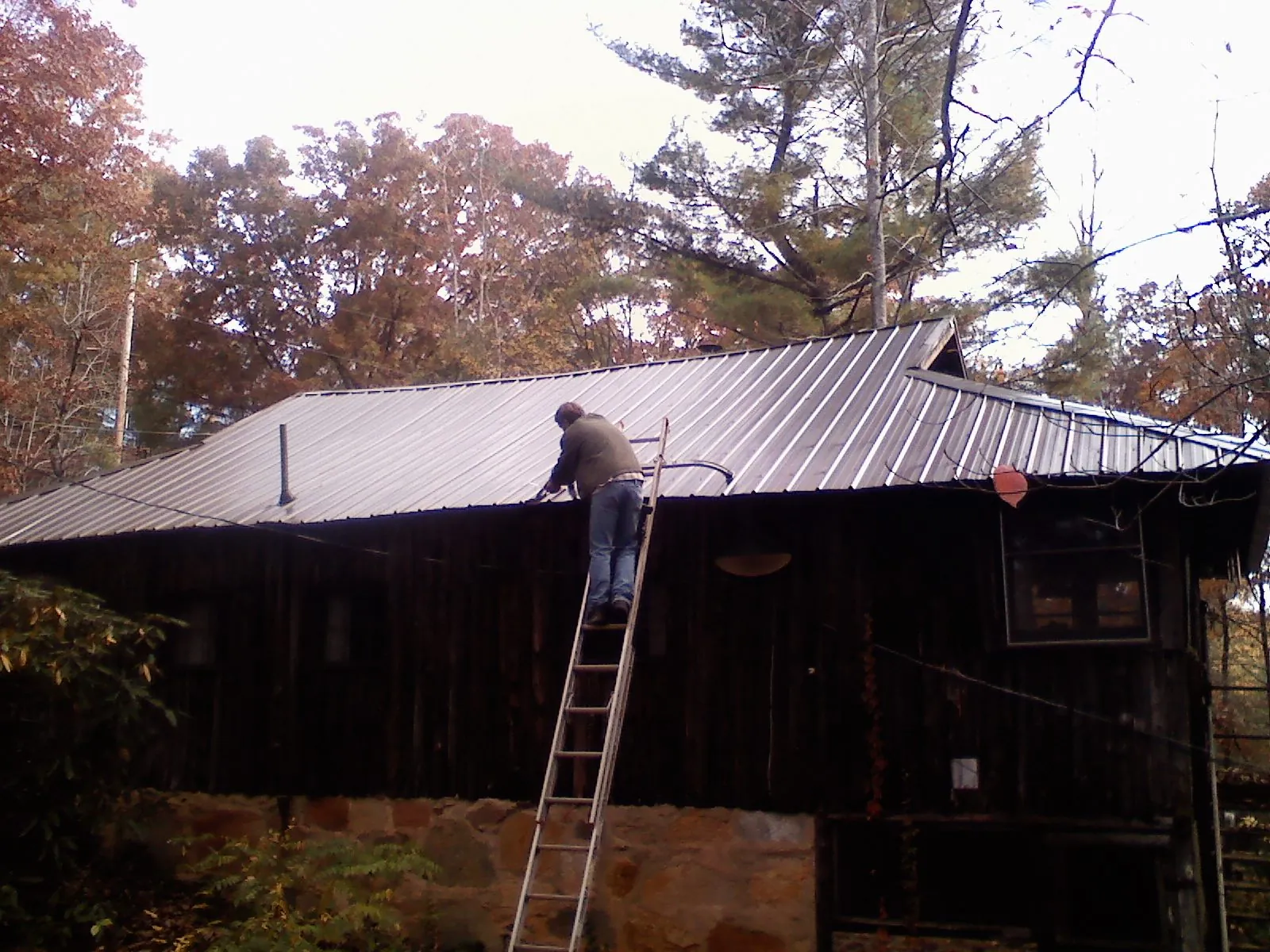 Roofer on a ladder working along the edge of a cabin metal roof in New Gretna