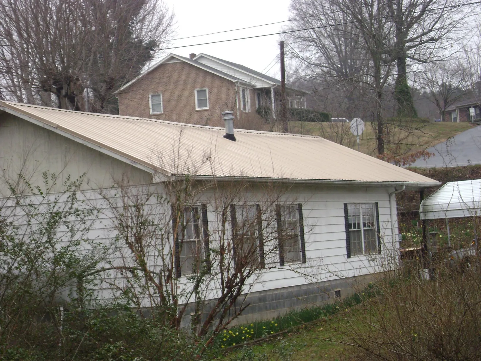 Tan metal roof on a white sided house set into a hillside — Commercial Roofing by Roofing Brothers in New Gretna