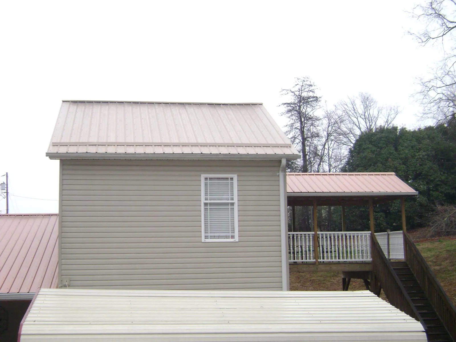 Tan metal roofs on a two story addition and attached porch, from a Roof Replacement job in New Gretna